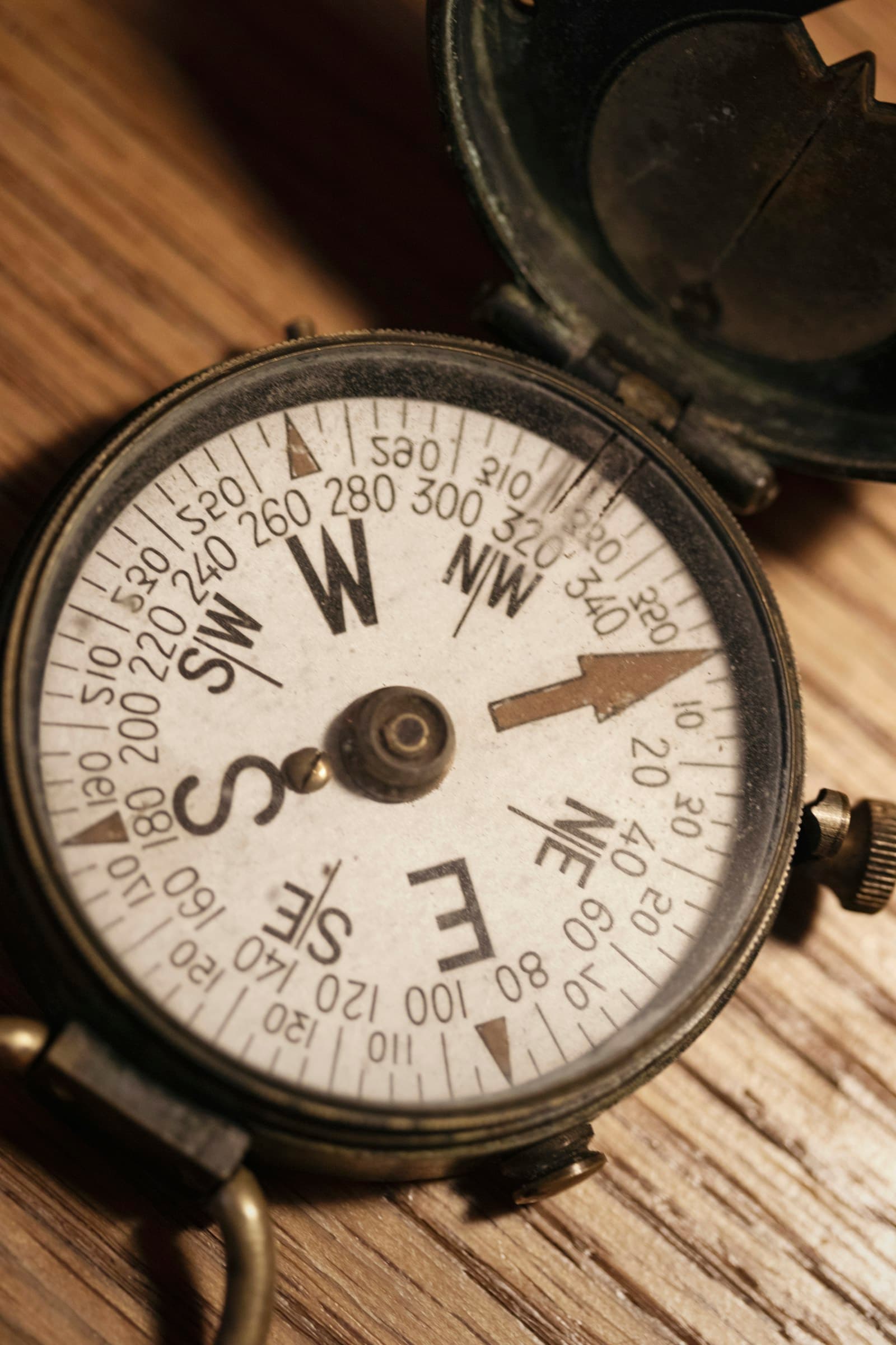 An antique brass compass resting on a wooden table, the needle settling on north