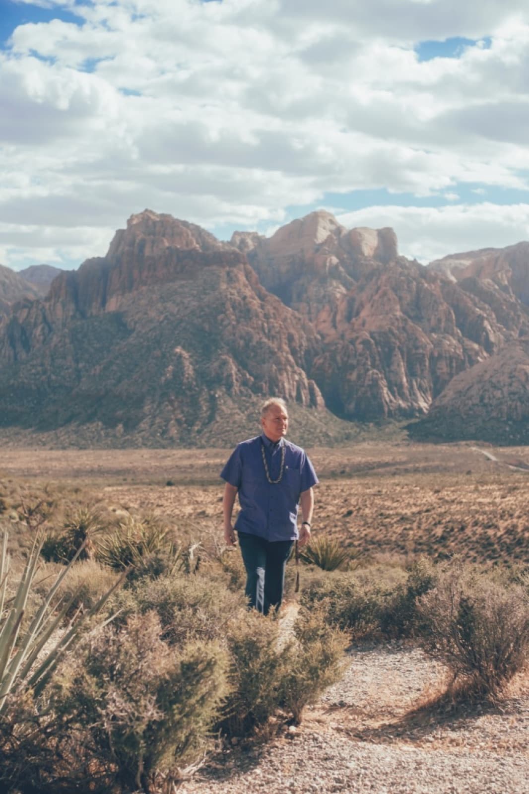 A man walking a desert path with red rock behind him