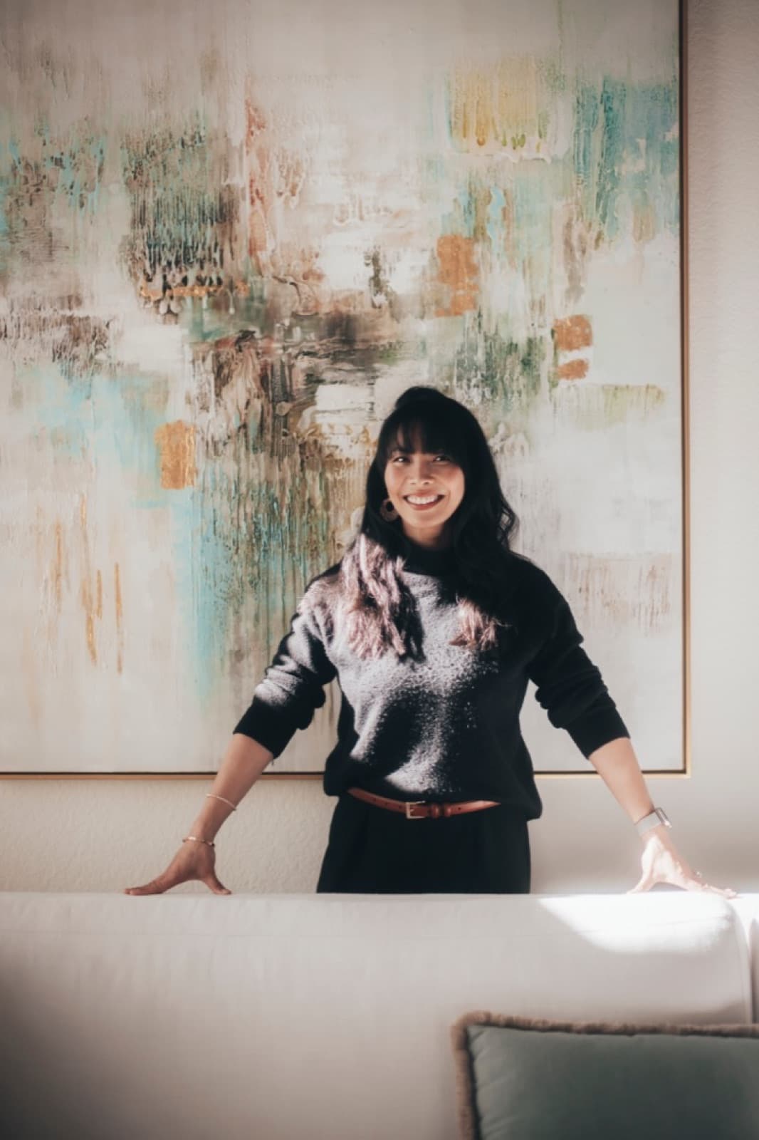 A woman standing behind a sofa in front of a large abstract painting